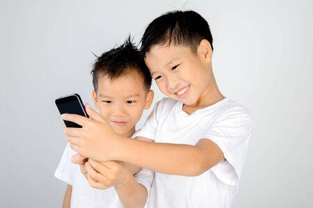 Two asian white shirt boy use smartphone for selfie together. On white background.の写真素材