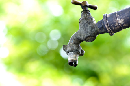 Close up old and grunge brass faucet and water drop on green bokeh from tree background. Water shortage concept.の写真素材