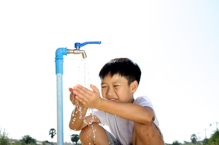 Close up Asian boy open metal blue water faucet on hot and dry empty land. Water shortage concept.の写真素材