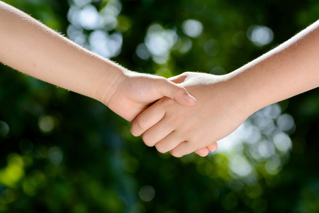 Close up two boy hands hold together on green bokeh background from tree leafの写真素材