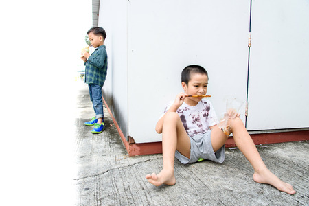 Younger Asian boy eat burger but poor boy eat chickent grill from bamboo stick at the corner of old building. Poor and hungry concept.の写真素材