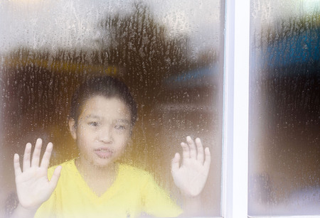 Young asian boy standing beside the window  with raindrop on the glass after raining with.