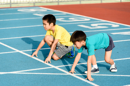 Young Asian boy prepare to start running on blue track in the stadium during day time to practice himself.の写真素材