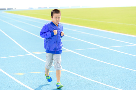 Young Asian boy running on blue track in the stadium in day time to practice himselfの写真素材