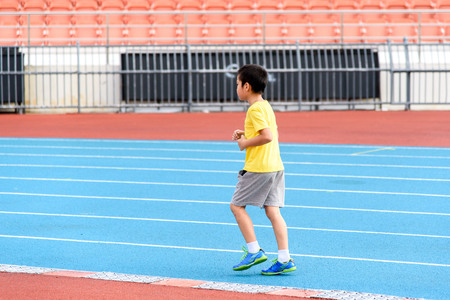 Young Asian boy running on blue track in the stadium during day time to practice himself.の写真素材
