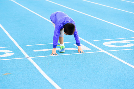 Young Asian boy running on blue track in the stadium during day time to practice himself.