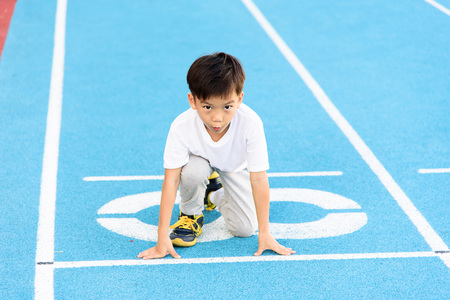 Young Asian boy running on blue track in the stadium during day time to practice himself.
