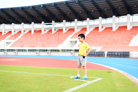 Young Asian boy standing on green football field in stadium during day time and feel relax.の写真素材