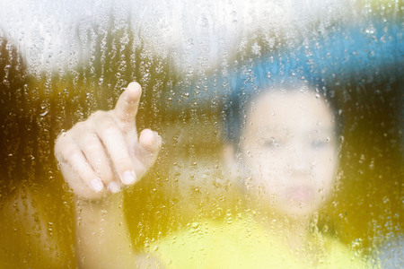 Young asian boy standing beside the window  with raindrop on the glass after raining with.の写真素材