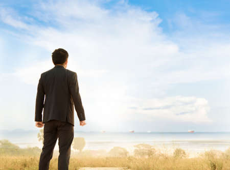 Warm tone. Business man standing on the mountain and look to the ocean with the container ship.の写真素材