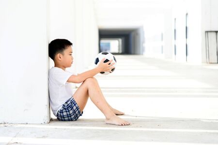 Lonely boy sit at the white building wth football.の写真素材