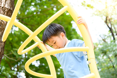 Young asian boy climb on the yellow bar  to exercise at out door playground under the big tree.の写真素材
