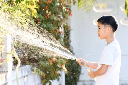 Young Thai boy spray water to the plant in his garden at home. Earth day concept.の写真素材