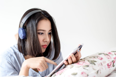 Selective focus on girl face that using blue headphone to listen music from mobile phone device. Relax and entertainment concept.の写真素材
