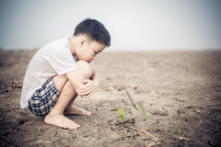 Young Thai boy planting little seedling on dry and crack empty land. Earth day concept.の写真素材