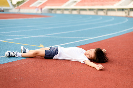 Young Asian boy tired and lay down on the running track.の写真素材