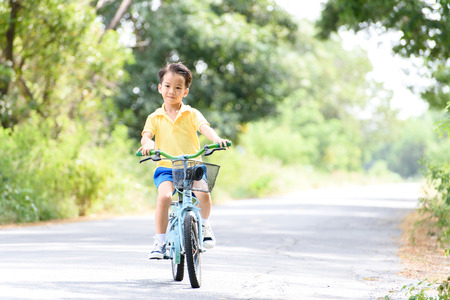 Young Asian boy ride a blue bicycle on the old road beside the tree and grass in summer time with warm sunlight.の写真素材