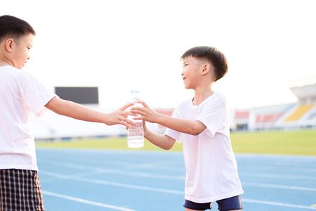 Running Asian boy taking bottle of water from another boy on the race track.の写真素材