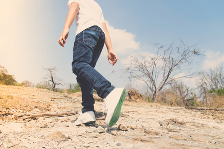 Vintage color, Kids leg in blue jean walking through the rough rocky land in the day time with strong sunlight. focus on shoe.の写真素材