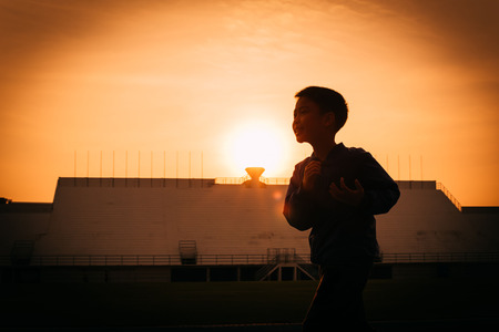 Silhouette and vignett border effect of Young boy in jacket running on track in the stadium against sunrise to practice himself.の写真素材