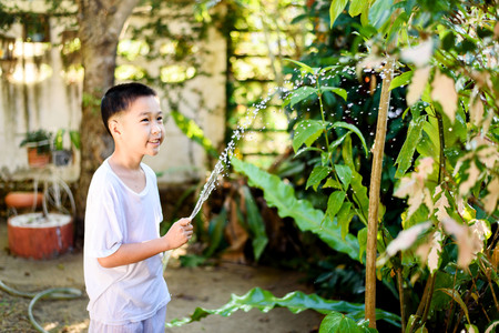 Young Thai boy spray water to the plant in his garden at home. Earth day concept.の写真素材