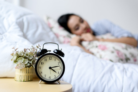 Selective focus on antique black alam clock in front of young and beautiful asian girl on the bed.の写真素材
