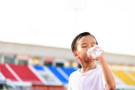 Young Asian boy drinking fresh water from plastic bottle after sport in stadium.の写真素材