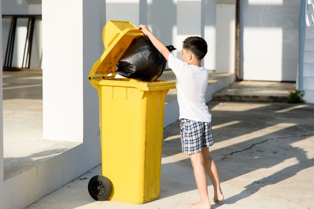 Young Asian boy carry garbage in plastic bag for eliminate in the yellow bin under the sunlighの写真素材
