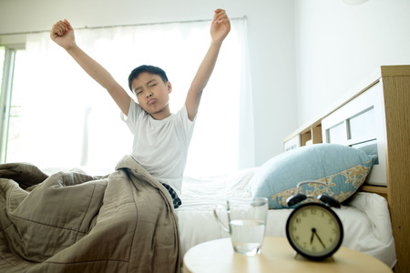 Selective focus on the glass of water in front of the young asian boy on the bed.の写真素材