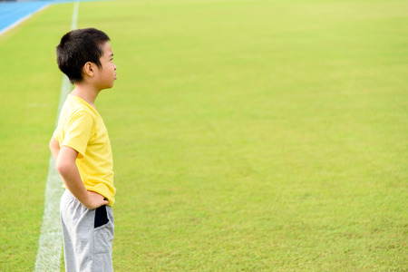 Young Asian boy standing on green football field in stadium during day time and feel relax.の写真素材