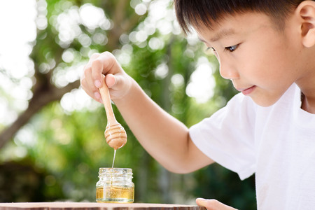 Young Thai boy interesting at honey comb from the small bottle in the garden.の写真素材