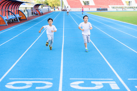 Young Asian boy running on blue track in the stadium during day time to practice himself.