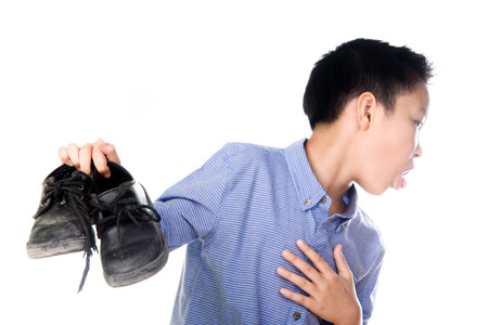 Selective focus on the old and dirty shoe, Young Asian boy feeling unhappy with bad smell black leather shoes on white background.の写真素材