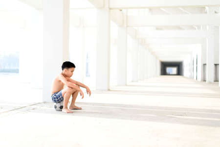 Young Asian boy sit on the old football alone in the white building.