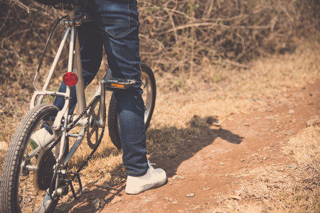 Vintage color, Selective focus at leg and shoe of Young boy wear blue jean ride an vintage color old bicycle on the stone rough road on the dry hill in summer time with strong sunlight.の写真素材