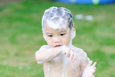 Selective focus on the eye of young asian boy take shower in the garden by a lot of soap foam on his body and head.の写真素材
