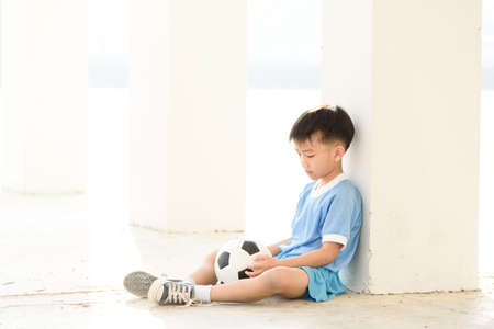 Lonely boy sit at the white building wth football.の写真素材