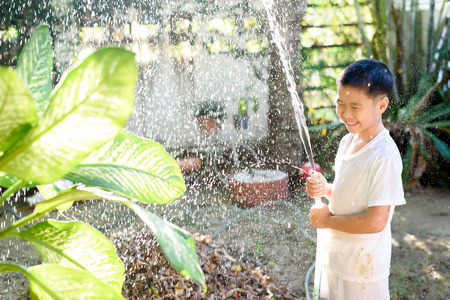Young Thai boy spray water to the plant in his garden at home. Earth day concept.の写真素材