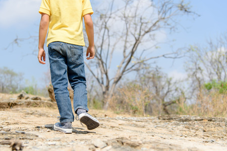 Kids in blue jean walking through the rough rocky land in the day time with strong sunlight.の写真素材