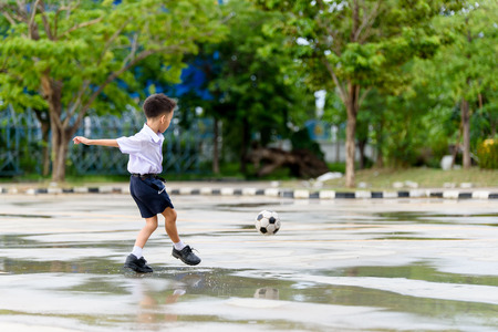 Boys in Thai student uniform black shoe play football on the concrete floor after the rainfall with the reflection.の写真素材
