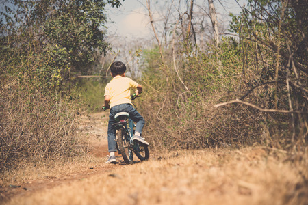 Vintage color, Young boy wear blue jean ride an vintage color old bicycle on the stone rough road on the dry hill in summer time with strong sunlight.の写真素材