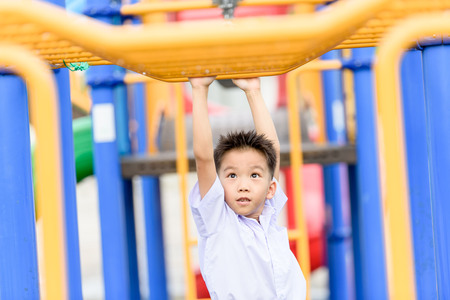 Young Thai student boy in school uniform play with the yellow bar at the playground.