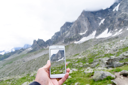 Hand holding smartphone taking photo of Aiguile du Chardonnet a beautiful view of Mont Blanc Massif , Chamonix France, Europeの写真素材
