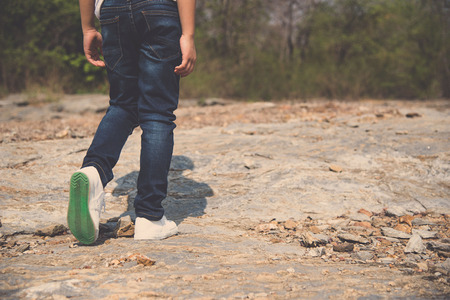 Vintage color, Kid leg in blue jean walking through the rough rocky land in the day time with strong sunlight.の写真素材
