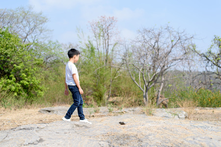 Young Asian Boy walking through the rough rocky land in the day time with strong sunlight.の写真素材