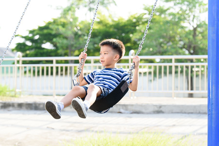 Young asian boy play a iron chain swinging at the playground under the sunlight in summer.の写真素材