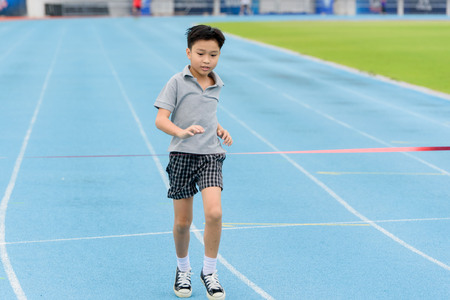 Selective focus at young Asian boy running on blue track to the finished line.