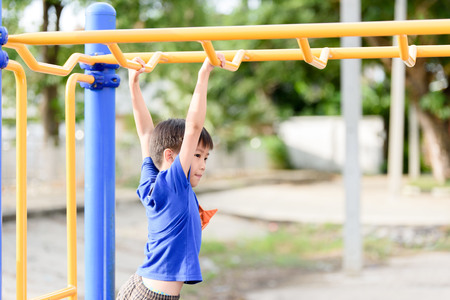 Young asian boy hang the yellow bar by his hand to exercise at out door playground