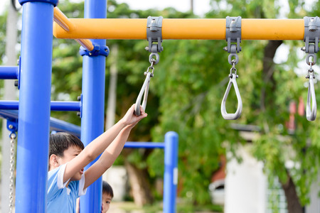 Young asian boy hang the yellow bar by his hand to exercise at out door playground
