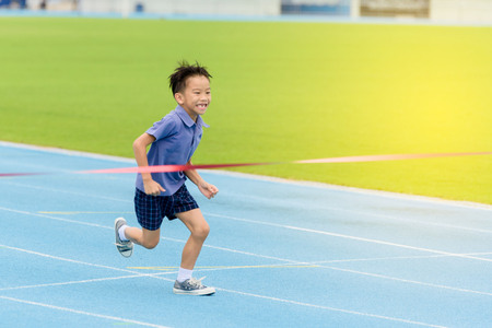 Selective focus at young Asian boy running on blue track to the finished line.の写真素材